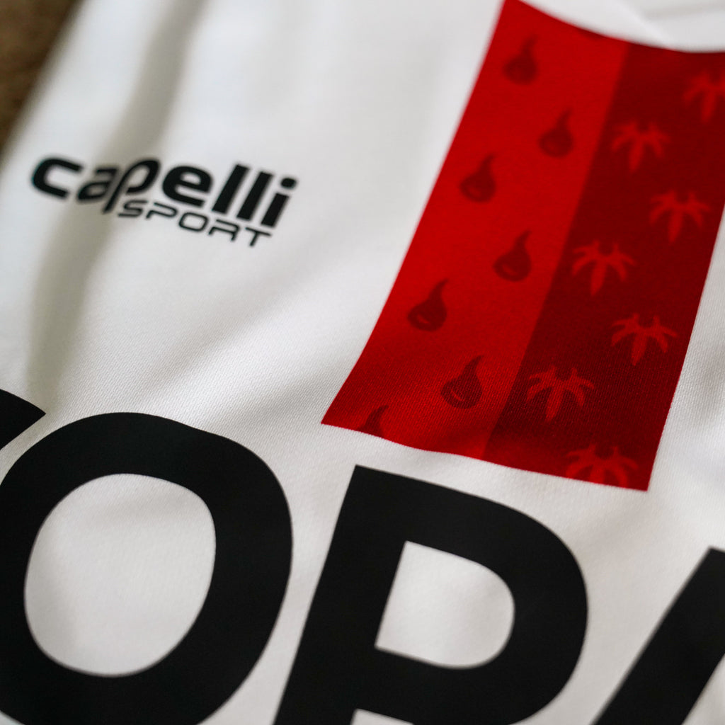 Close-up of a sports jersey with 'capelli sport' branding and a logo on a white background.