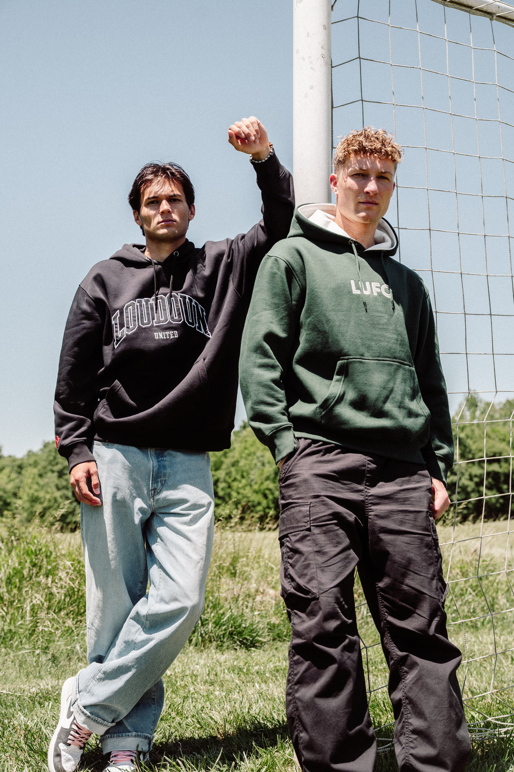Two individuals wearing hoodies with 'LOU' branding in a grassy outdoor setting.