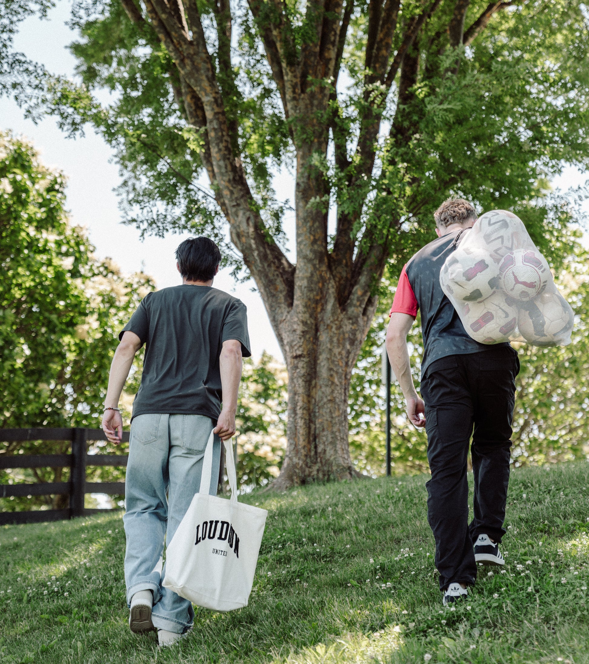 Two people walking outdoors with bags, one carrying a large bag of items. 
