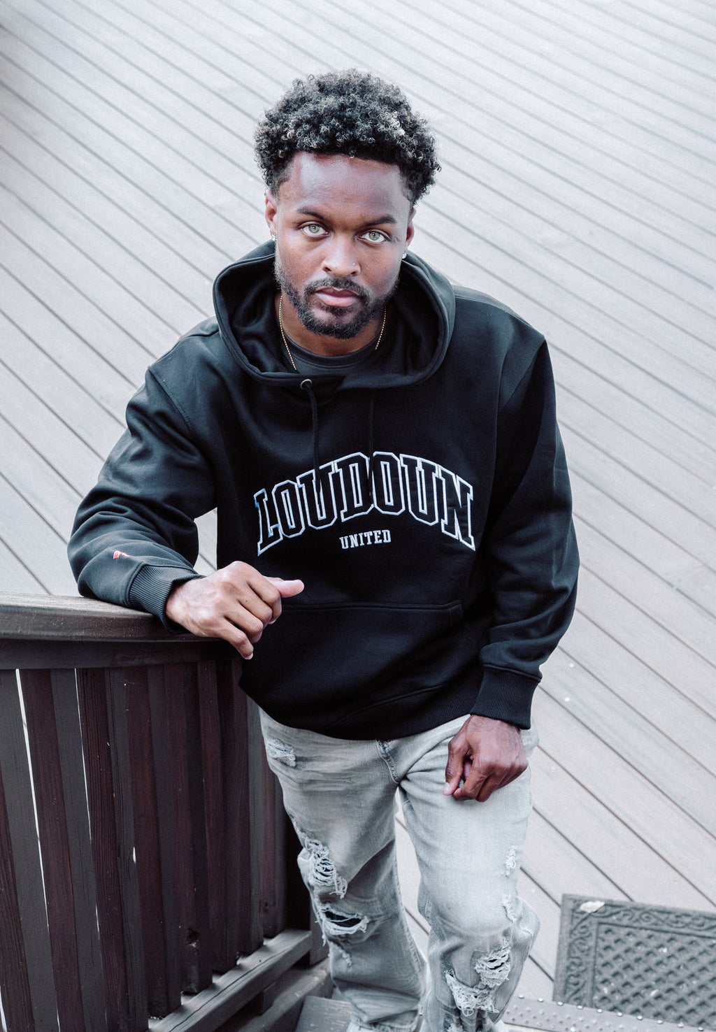 Person wearing a black hoodie with 'LOUDOUN UNITED' text, standing on steps against a light-colored wall.